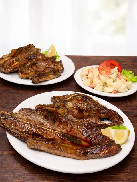 Costillas a la plancha con limón y un plato de ensalada rusa