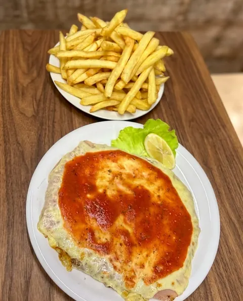 Milanesa napolitana gratinada con salsa, al lado de un plato de papas fritas