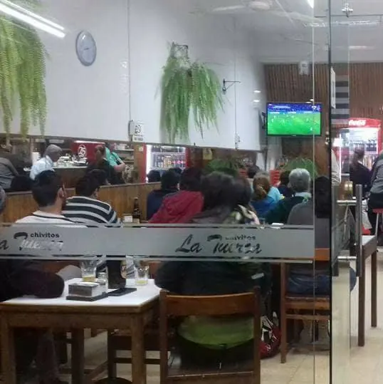 Salón lleno de clientes mirando un partido, con el logo de La Tuerca en el vidrio